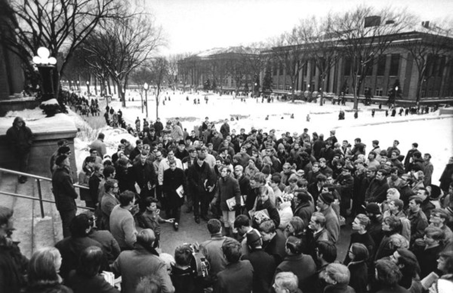 Historic image of students in the 1960s gathered around the steps of Morrill Hall listening to a speech.
