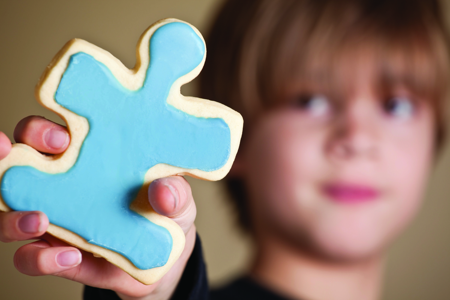 Boy holding blue frosted cookie that's shaped like a puzzle piece